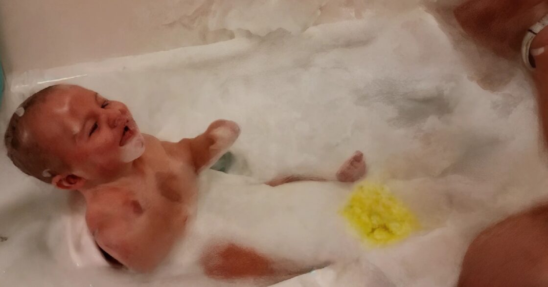 De schattige baby begint te lachen als zijn vader schuim blaast in bad wat een aanstekelijke lach